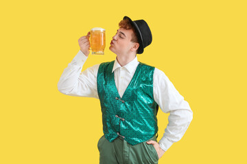 Young man in traditional German clothes with beer on yellow background