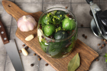 Jar with fresh cucumbers for preservation on grey tile background