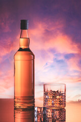 Bottle of whiskey in a cloudy sky at sunset.