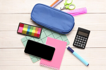 Mobile phone with calculator and different stationery on white wooden background