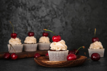 Plate with tasty cherry cupcake on black background
