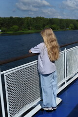 Fototapeta na wymiar A girl with long hair stands on the deck of the ship and looks at the shore.