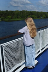 Fototapeta premium A girl with long hair stands on the deck of the ship and looks at the shore.
