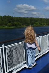 Fototapeta premium A girl with long hair stands on the deck of the ship and looks at the shore.