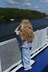 Fototapeta na wymiar A girl with long hair stands on the deck of the ship and looks at the shore.