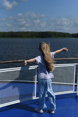 Fototapeta premium A girl with long hair stands on the deck of the ship and looks at the shore.