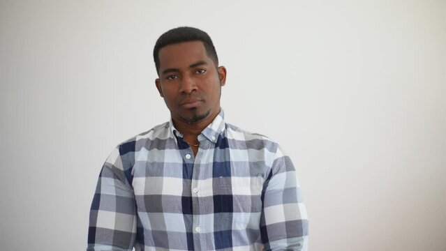 Studio portrait of cheerful cheerful young african american man wearing plaid shirt standing posing on white isolated background, smiling looking at camera. Shooting in slow motion.