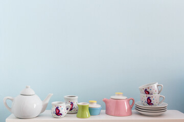 
Adorable collection of doll tea sets on shelf against pale blue background
