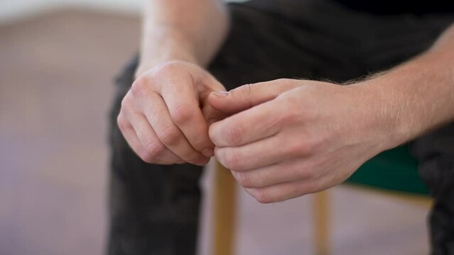 Close-up hands of unrecognizable nervous young man sharing traumatic experience at therapy meeting during group psychotherapy session, slow motion. Concept of group consulting of mental health problem