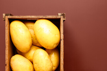 Wooden box with raw potatoes on brown background