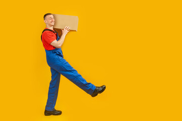Worker man holding delivery courier box and taking step, goods delivery. Studio photo on yellow background. Copy space, mock up