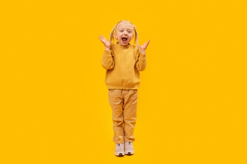 Little girl is screams or surprised. Full-length portrait of preschool girl in yellow suit on yellow background.