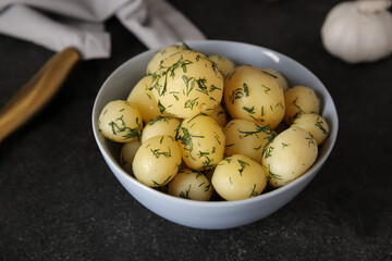 Bowl with boiled baby potatoes on black background