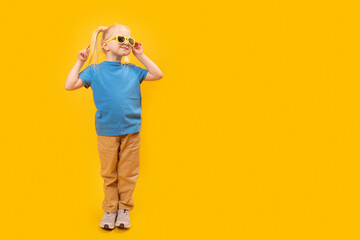 Happy funny blond little girl wear sunglasses and blue t-shirt on yellow background. Copy space, mock up