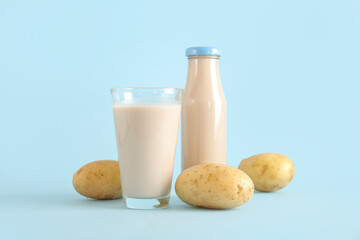 Bottle and glass of tasty potato milk on blue background