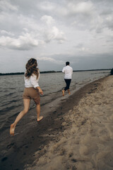 A guy and a girl run barefoot on a wet beach near the sea in summer