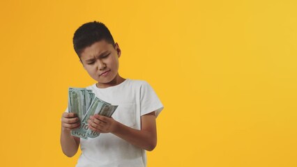 Young boy standing, counting the banknotes and carefree smiling on a yellow background. Concept of child financial literacy and upbringing of money responsible attitude