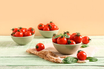 Bowls with fresh cherry tomatoes and basil on green wooden table