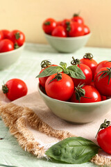Bowls with fresh cherry tomatoes and basil on green wooden table