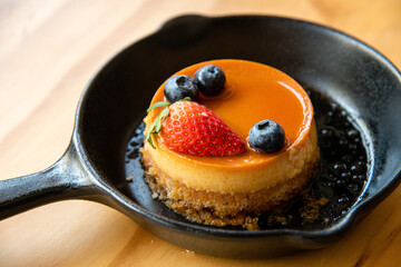 close up of a cheese cake in small serving pan topped with strawberry on wooden table