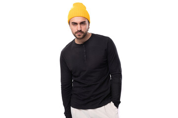 young brunette confident male model with a beard dressed in a black jacket and a yellow hat