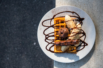 a waffle ontop with banana and chocolate icecream and chocolate bar topped with chocolate sauce