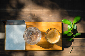 a glass of water and a mug of coffee on the cutting board with white cloth on wooden table