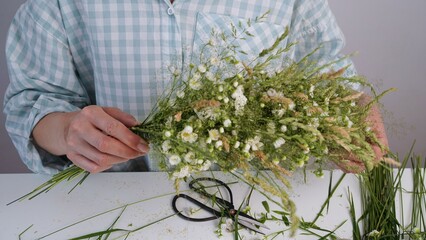 Floristic master class on weaving flower wreath for feast of Ivan Kupala.Woman weaves wreath of fresh field herbs and flowers,pagan symbol,solstice day.Rustic style.Wreath of daisies and herbs,summer.
