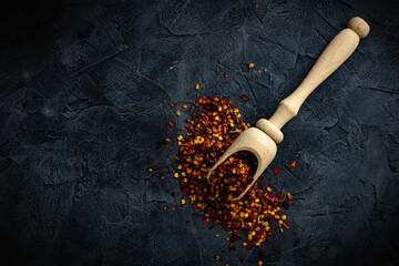 Dried red pepper flakes with wooden spoon isolated on dark background. Top view