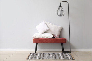 Bench with white pillows and standard lamp near white wall