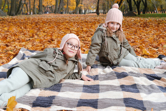 Two twin sisters lie on a blanket in the autumn park - Powered by Adobe