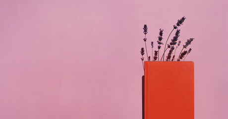 Orange book or notebook with lavender flowers inside on pink background with long shadows....