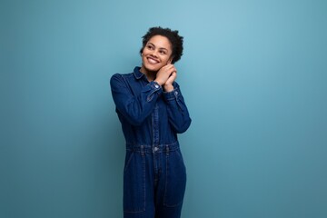 young hispanic brunette woman with fluffy curly hair posing in blue denim suit