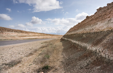 Obraz premium Road in the steppes of Kazakhstan among the layered hills of the Ustyurt plateau, on a spring cloudy day