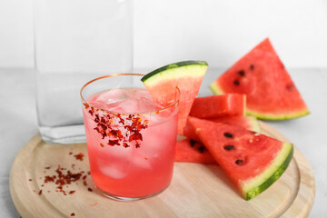 Board with glass of tasty watermelon cocktail and bottle on white tile background