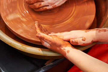 Teaching a child to make pottery from red clay. Clay pottery hands close up working on wheel...