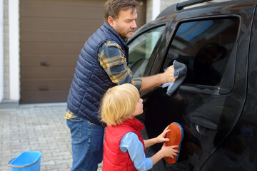 Preschooler boy helping his father washing family car. Little dad helper. Family with children...