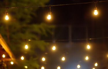 Photo of string lights hanging in restaurant or cafe in the garden at evening time. Fashion decoration with bulbs for night summer party. Outdoor electric lamps