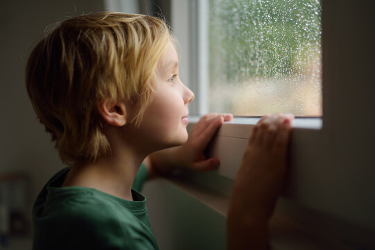 Portrait of preteen boy standing at the window. Child watching the rain outside.