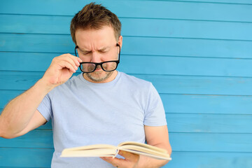 Portrait of mature man with big black eye glasses trying to read book but having difficulties...