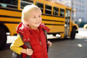 Cute elementary student with schoolbag on background of usa yellow school bus
