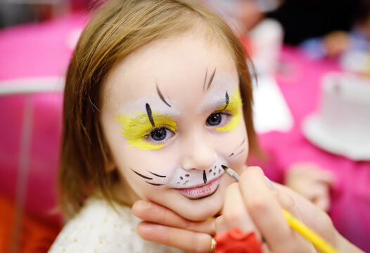 Face painting for cute little gorl during kids merriment. Face paint for "Animals" theme on birthday party. Preschooler kids celebrating party in entertainment center.
