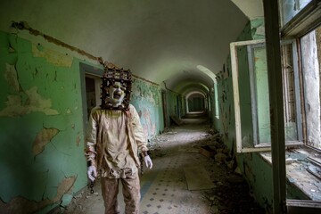 Fototapeta na wymiar Ghost of maniac with cage on his head walking down corridor of abandoned asylum.