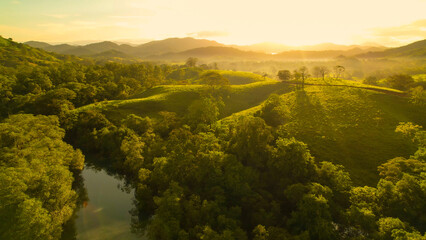 AERIAL: Morning sunbeams illuminate picturesque hilly landscape with calm river - obrazy, fototapety, plakaty