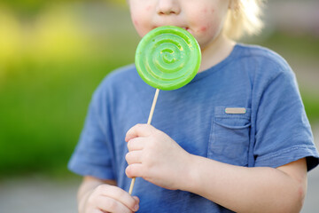 Child with allergic reaction eating big green lollipop. Unhealthy sweet food for young kids....