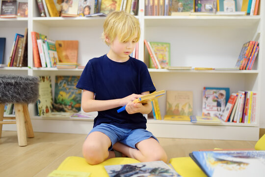 A preteen boy leafing through a book while sitting at the bookshelves in a school library or bookstore. Smart kid reading adventure book
