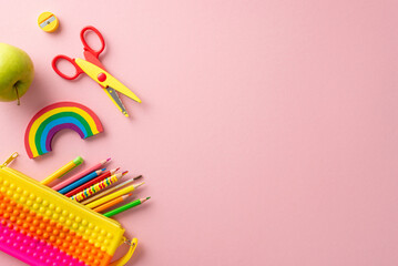 Classroom essentials. Overhead shot of lively materials: pop it pencil pouch, art pencils, rainbow plasticine, scissors, sharpener, and green apple on pastel pink background. Space for text or advert