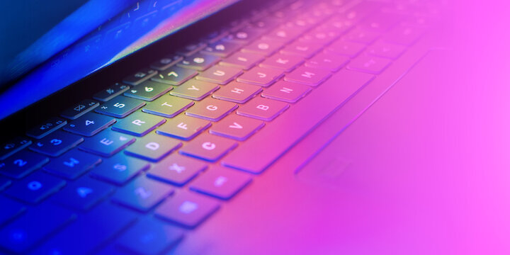 Laptop keyboard with vibrant hues illuminating the keys, wallpaper with colorful lights casting on the computer keyboard, dynamic technology concept, close-up, copy space