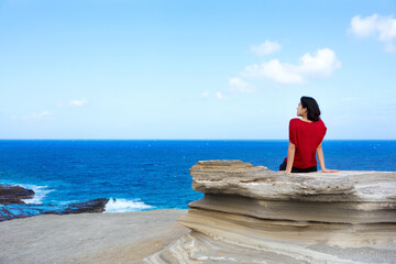 Young woman sitting on large rock cliff  by Hawaiian  ocean