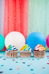 Three rainbow color cupcakes on colorful pink, green and blue background with air balloons